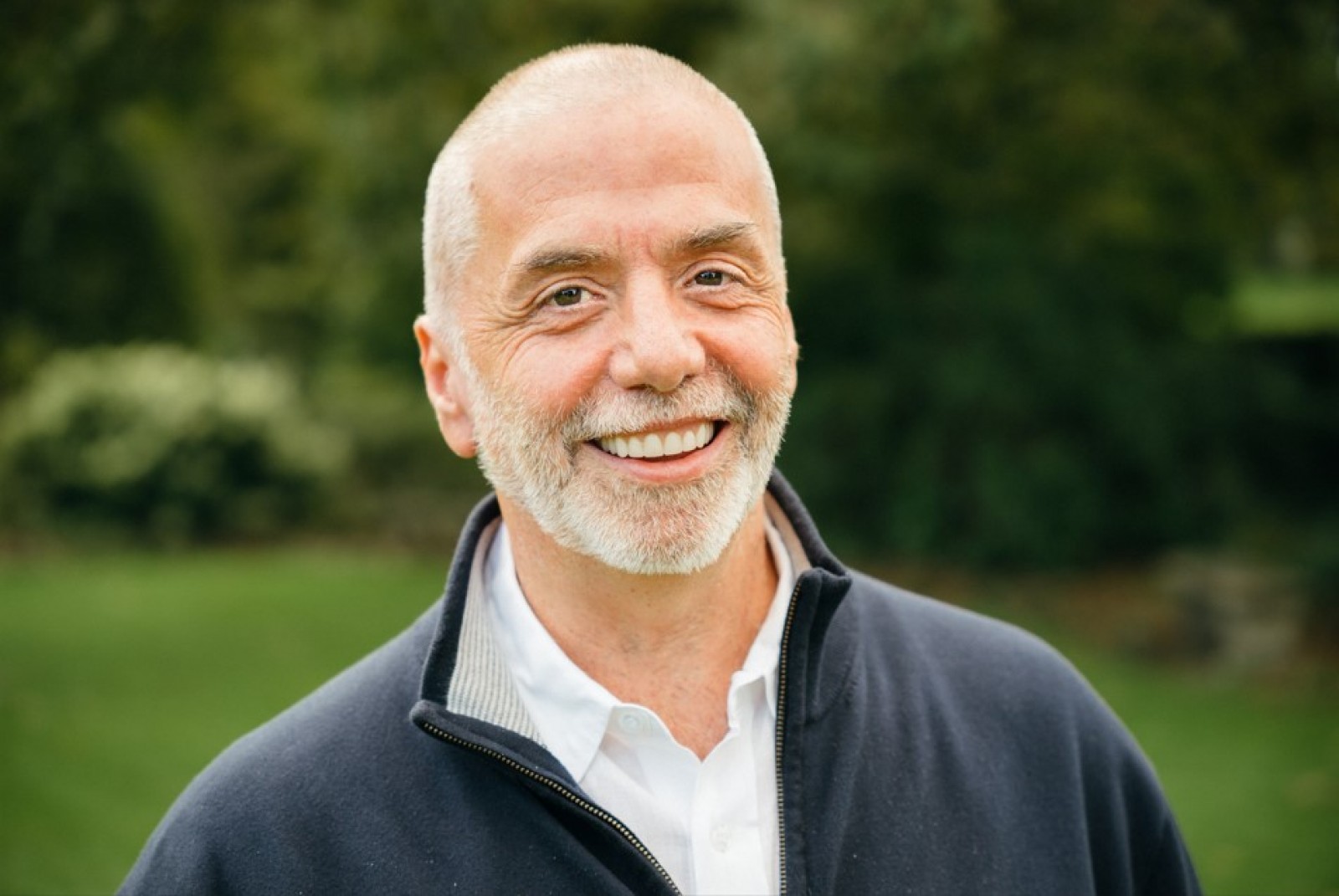 A photograph of Dr Joe Tucci. He is smiling. The background is green. alt=